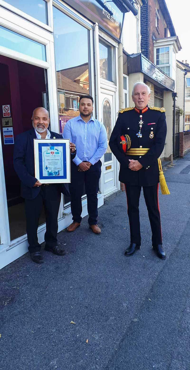 Three people outside shop holding award.