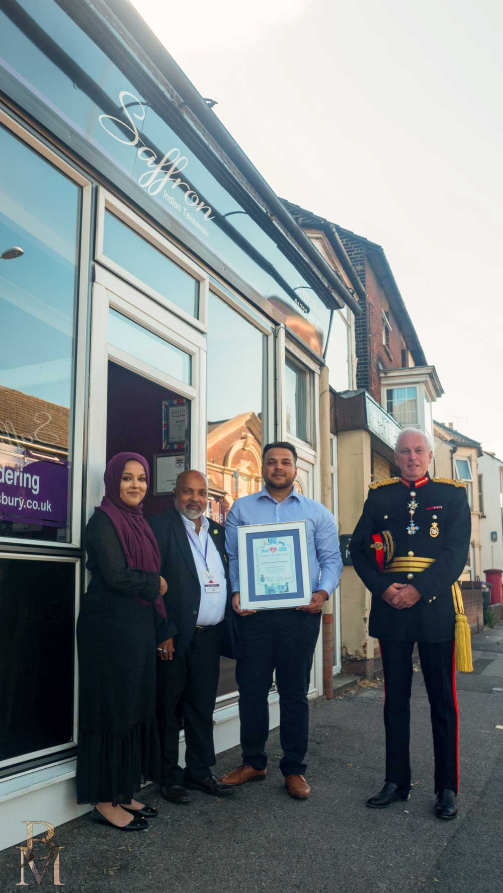 Three people outside shop holding award.